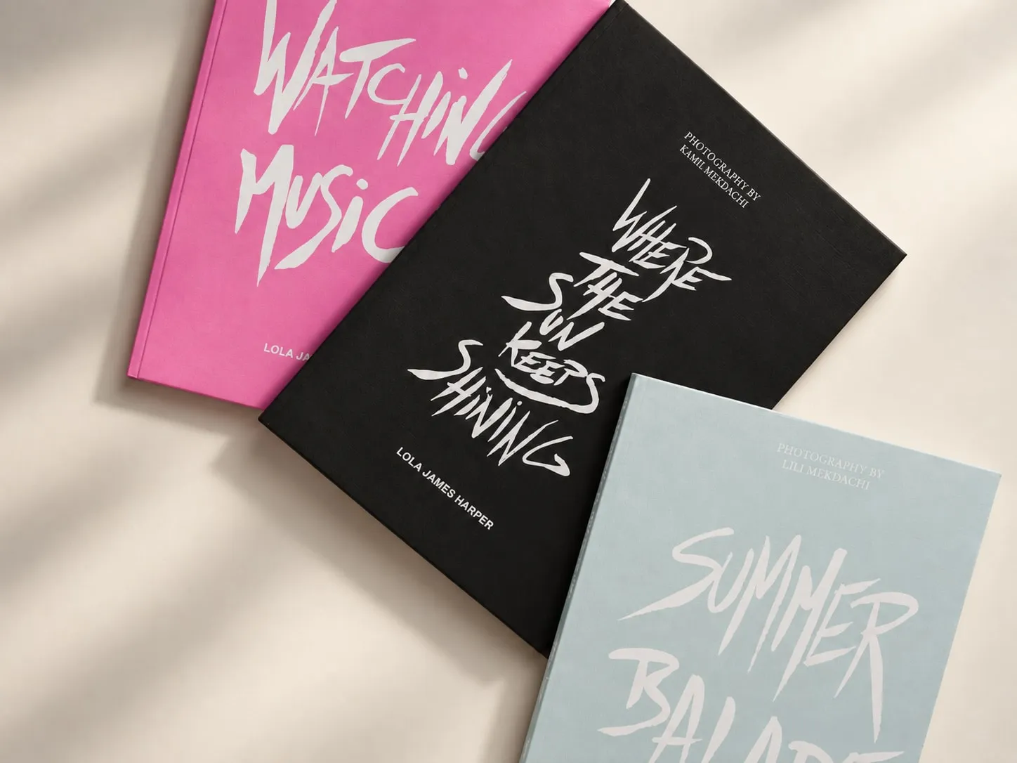 La composition des trois livres avec la couverture centrale noire, sur un fond crème traversé d'ombres de feuillage.